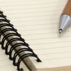 A spiral-bound notebook with cream pages, accompanied by a metallic pen with a wooden grip.