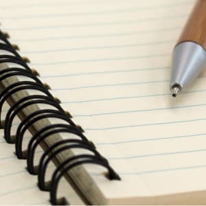A notebook with a spiral binding and lined pages, accompanied by a silver-tipped pen.