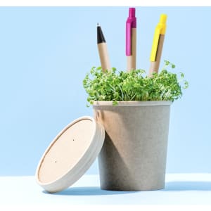 A pot with green sprouts contains three writing utensils: a black pen, a pink pen, and a yellow highlighter.