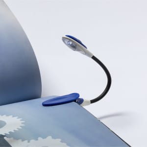 A blue and white Lektura Lamp with a flexible neck, attached to an open book, providing light for reading.