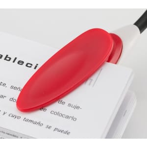 A red Lektura Lamp positioned on an open book, featuring a white base and flexible arm.