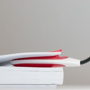 A red and white Lektura Lamp rests on top of a stack of documents against a neutral background.