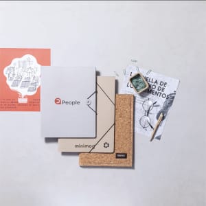 A collection of notebooks and a cork folder in natural tones, accompanied by stationery items like a pen and paper clips.