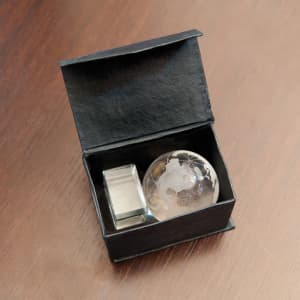 A decorative box containing a globe paperweight and a small rectangular item, both with a sleek design.