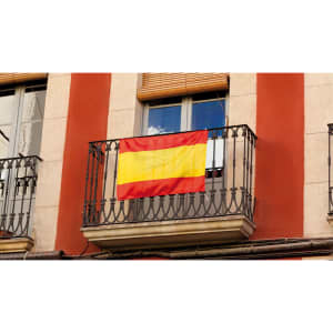 A red and yellow Spanish flag hanging from a balcony with ornate metal railings.