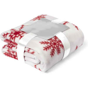 A folded blanket in white with red snowflake patterns, secured with a ribbon and featuring a logo.