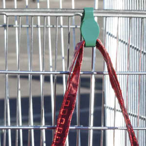 A green plastic holder clips onto a metal cart, securing a red strap in place. The background features a wire grid.