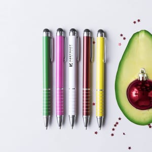 A collection of five stylus touch ball pens in green, pink, white, red, and yellow, alongside a festive avocado decoration.