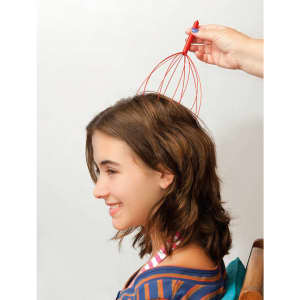 A red and silver head massager is being used on a girl’s head, providing relaxation. The background is neutral.