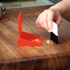 A red dustpan and brush set being used to clean crumbs from a wooden surface.