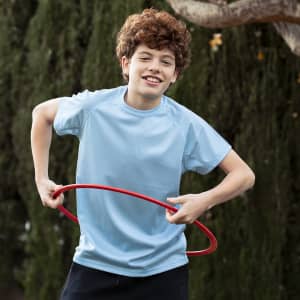 A boy wearing a light blue t-shirt is playing with a red hula hoop outdoors.