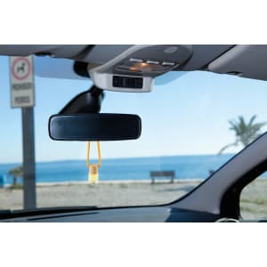 A yellow air freshener hanging from a car’s rearview mirror, with a scenic coastal view outside the window.