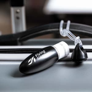A black luggage tag with a branding logo, featuring a transparent attachment cord.
