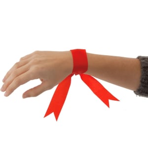 A red multipurpose bracelet with long, flowing ribbons is worn on a wrist. The hand is partially visible, showcasing the accessory.