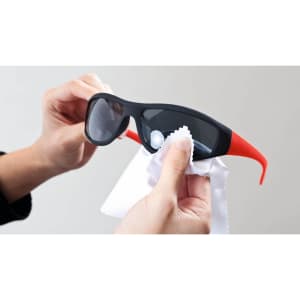 A black and red pair of sunglasses being cleaned with a white cloth, featuring a logo.