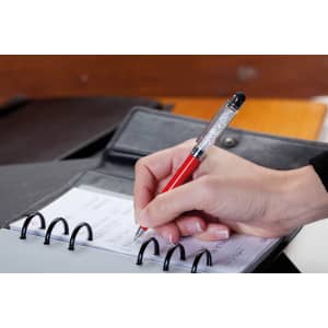 A red Globix Stylus Touch Ball Pen is held above a notebook with spiral binding and a black folder in the background.