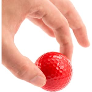 A red golf ball held between fingers, featuring a textured surface typical of golf balls.
