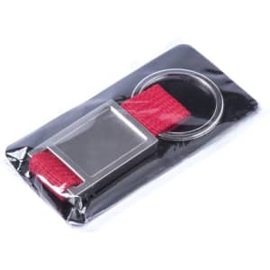 A metal keyring with a rectangular silver pendant and a red fabric strap, packaged in plastic.
