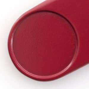 A red keyring with a smooth, round surface and a slight indentation. It includes a logo but no text is visible.