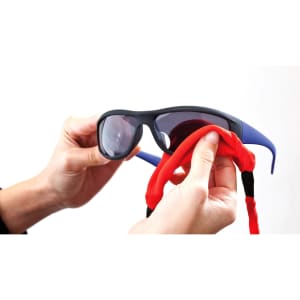 A pair of sunglasses held by hands, featuring a red and black multipurpose glasses strap.