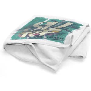 A folded white towel with a graphic design featuring colours like teal and palm trees, and it includes a logo.