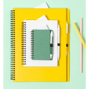 A set of notebooks in yellow and white, featuring a green notebook, pens, and pastel straws on a mint green background.