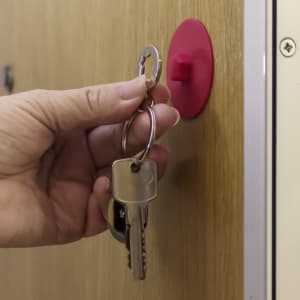 A hand holding a keyring with keys, attached to a red wall-mounted hook.