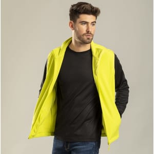 A man is wearing a bright yellow vest over a black long-sleeve shirt, set against a neutral background.