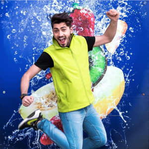 A man in a bright green vest jumps against a blue background featuring splashes of fruit. The vest has a logo.