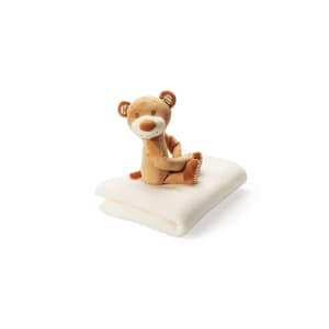 A soft, cream-coloured blanket with a plush teddy bear sitting atop it, featuring a cute design and friendly expression.