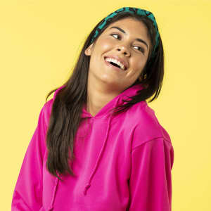 A woman smiles while wearing a vibrant pink hoodie, complemented by a green headband, against a yellow background.