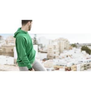 A green hoodie worn by a man standing against a backdrop of a city and ocean. The hoodie features a logo.