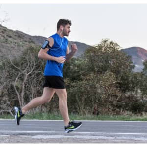 A person jogging along a road wearing a blue sleeveless shirt and black shorts, with earphones and a fitness armband.