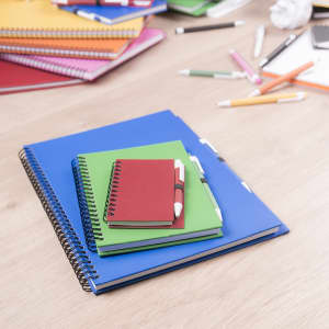 A stack of colourful notebooks in blue, green, red, and orange, arranged on a wooden surface.