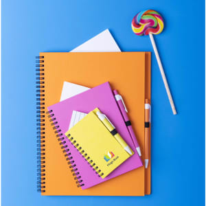 A collection of colourful notebooks in orange, pink, and yellow, with pens and a lollipop on a blue background.