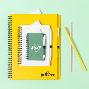 A green notebook and a stack of yellow notebooks on a mint green background, with two pens and colourful straws.