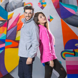 A grey polar fleece jacket worn by a man and a pink polar fleece jacket worn by a woman against a colourful mural background.
