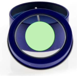 A blue candle tin with a transparent lid, revealing a green candle inside. The tin has a logo.