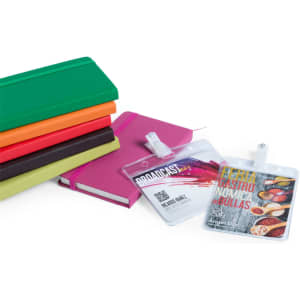 A stack of notebooks in various colours with two transparent ID badges displayed in front, featuring clips for attachment.