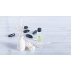 A ceramic diffuser in white with reed sticks, accompanied by green essential oil and two decorative balls on a light background.