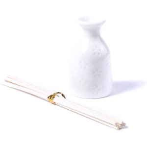 A white aromatic diffuser with a floral design accompanied by a pair of wooden sticks.
