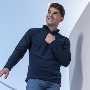 A young man wearing a navy blue polar fleece jacket, smiling while standing outdoors. The jacket features a zip neck design.