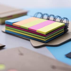 A sticky notepad with vibrant pink, green, blue, and orange notes stacked in a spiral-bound format.