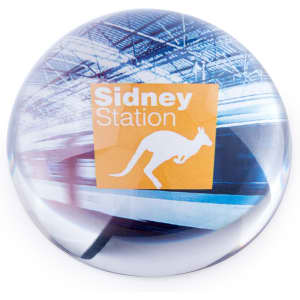 A round paperweight featuring a colourful image of a train station with a kangaroo silhouette and logo.