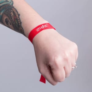 A red bracelet is worn on a wrist, featuring a logo. The wrist has a tattoo visible beside the bracelet.
