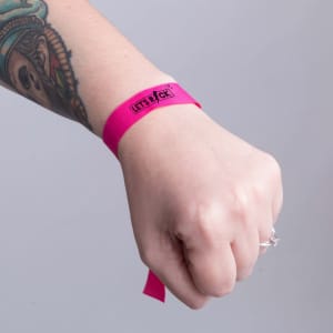A pink wristband is worn on a tattooed wrist, featuring a logo on the band.