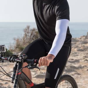 Duttier Arm Sleeves in white worn by a cyclist, paired with a black short-sleeve top and cycling shorts.