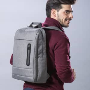 A grey backpack is worn on the back of a smiling man dressed in a burgundy sweater, featuring a zippered pocket.