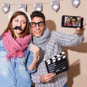 A novelty photo set featuring a couple with props like a fake moustache and glasses, holding a clapperboard and posing for a selfie.