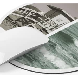 A round mousepad featuring a split design of a lifeguard tower and ocean waves in muted colours.
